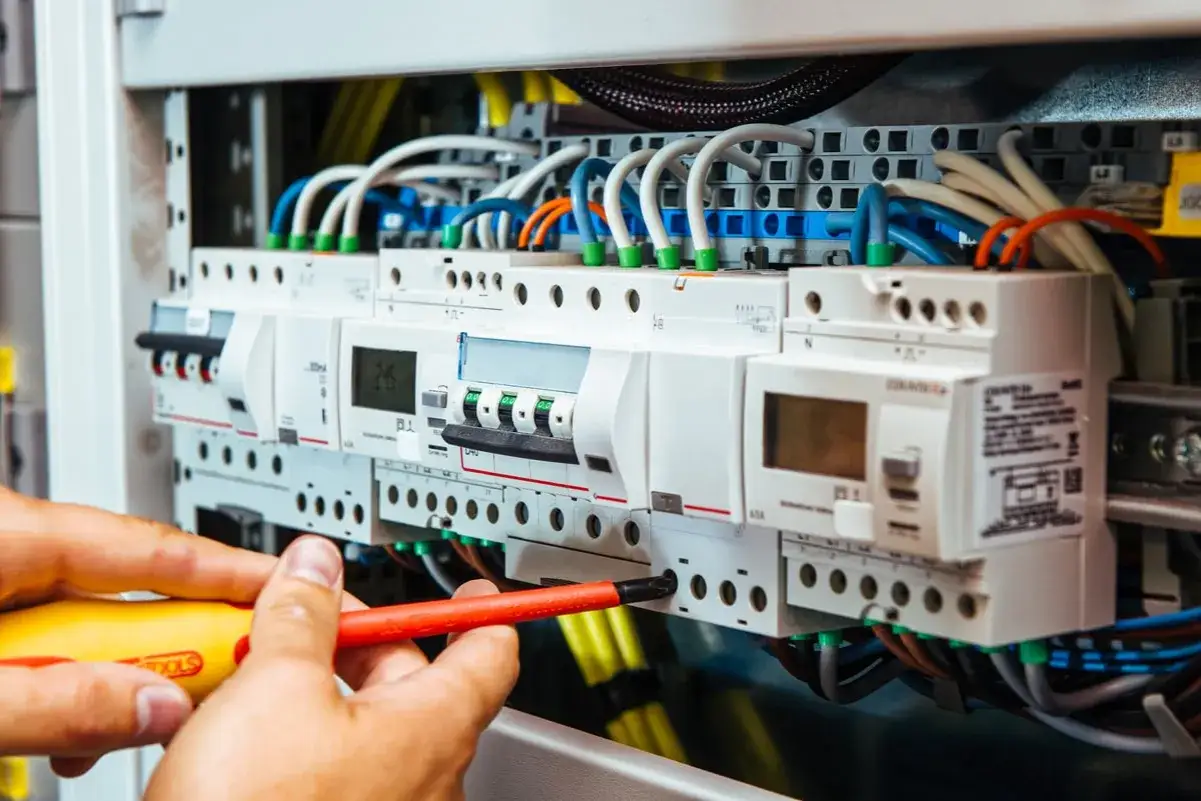 Installazione wallbox: mani esperte con cacciavite lavorano su un quadro elettrico con interruttori e cavi colorati.