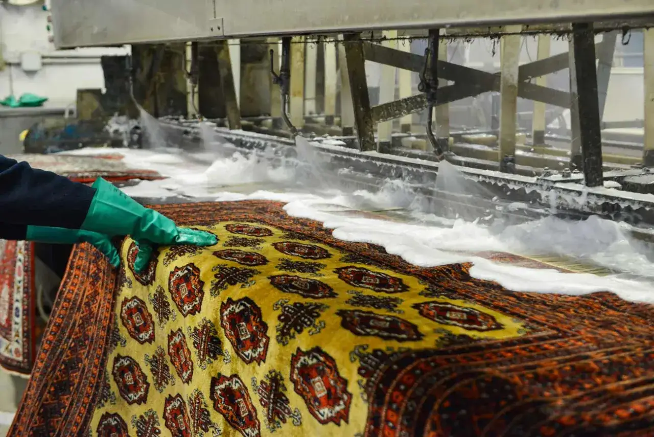 Un tappeto persiano viene lavato in una macchina industriale, con schiuma e getti d'acqua che ne puliscono le fibre.