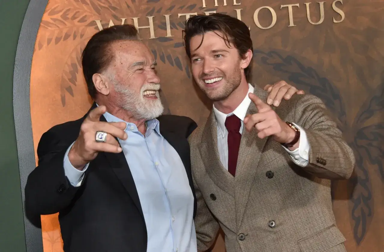Arnold Schwarzenegger i Patrick Schwarzenegger śmieją się i wskazują palcami, wyglądając jakby dzielili się zabawną historią.