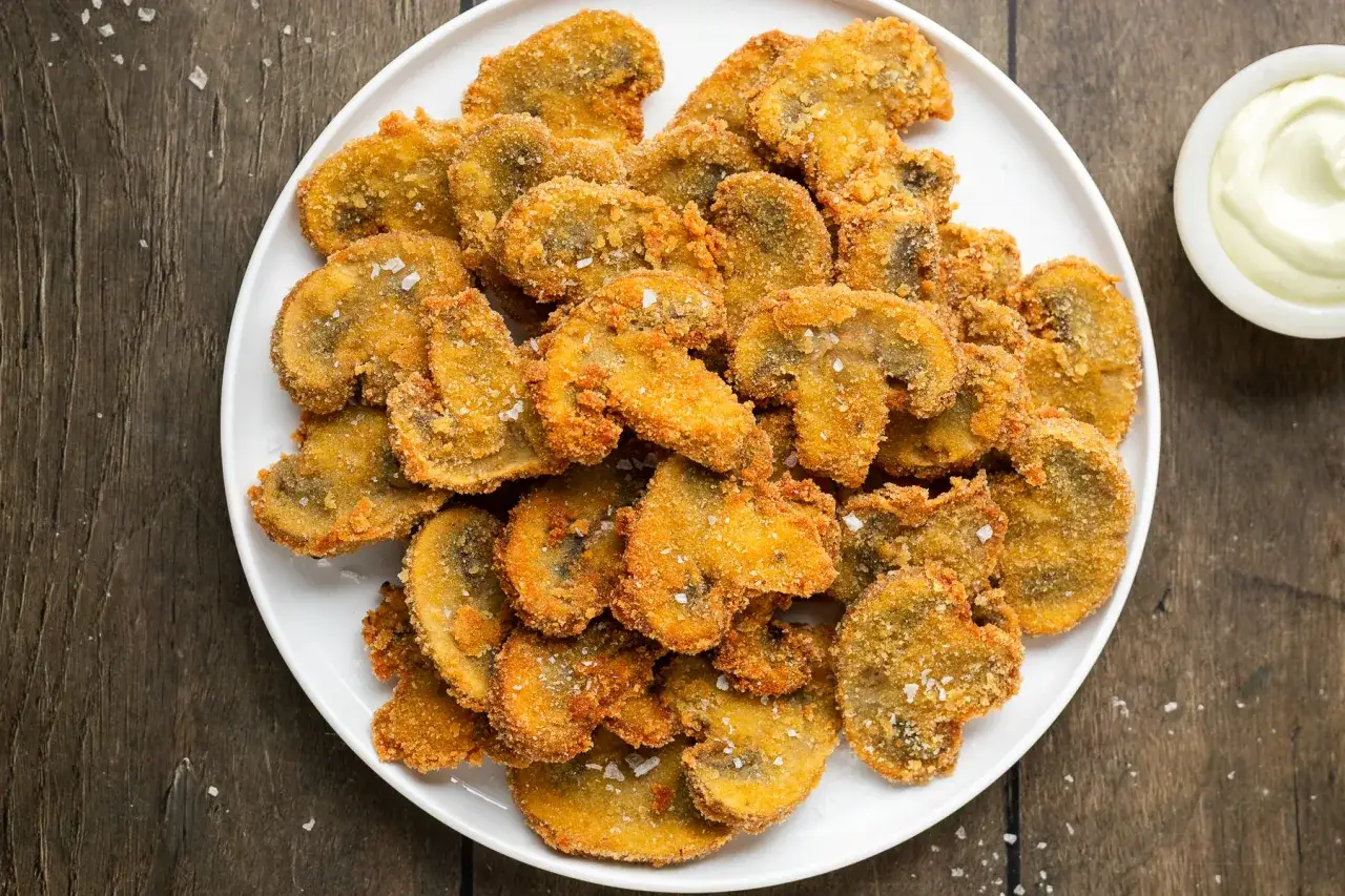Piatto di funghi fritti dorati e croccanti, cosparsi di sale grosso, pronti per essere gustati con una salsa cremosa.