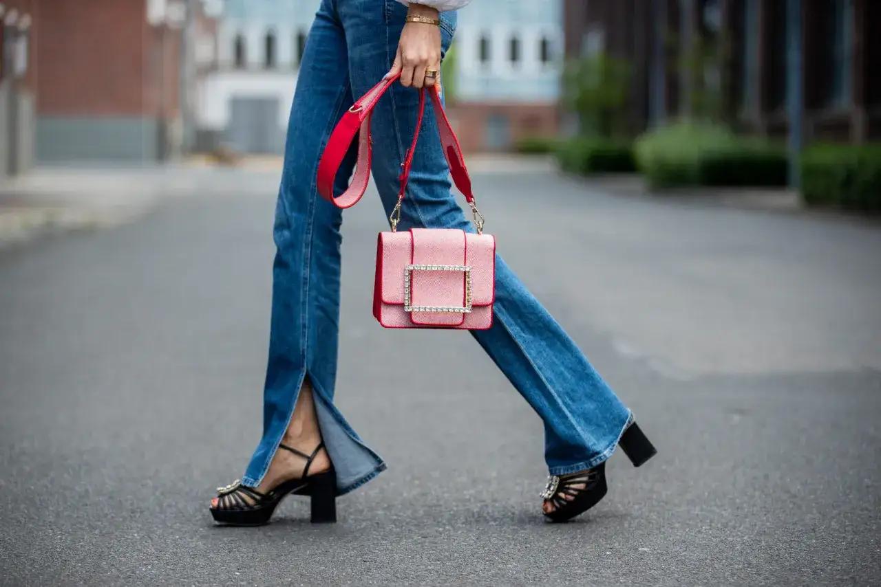 Kobieta w jeansach bootcut i sandałach na obcasie, z czerwoną torebką.