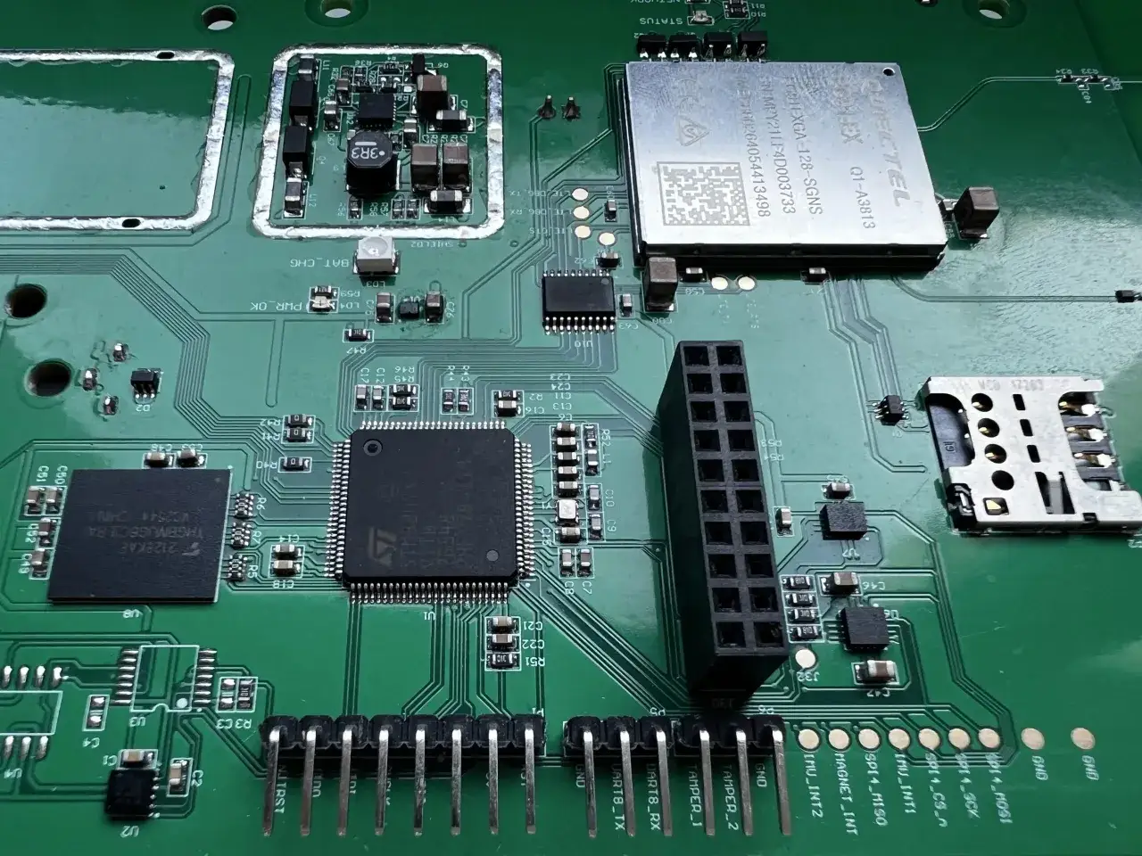Zielona płyta z elementami elektronicznymi, w tym procesorem i modułem komunikacyjnym. Widać złącza, kondensatory i rezystory, a także element przypominający oscylator.