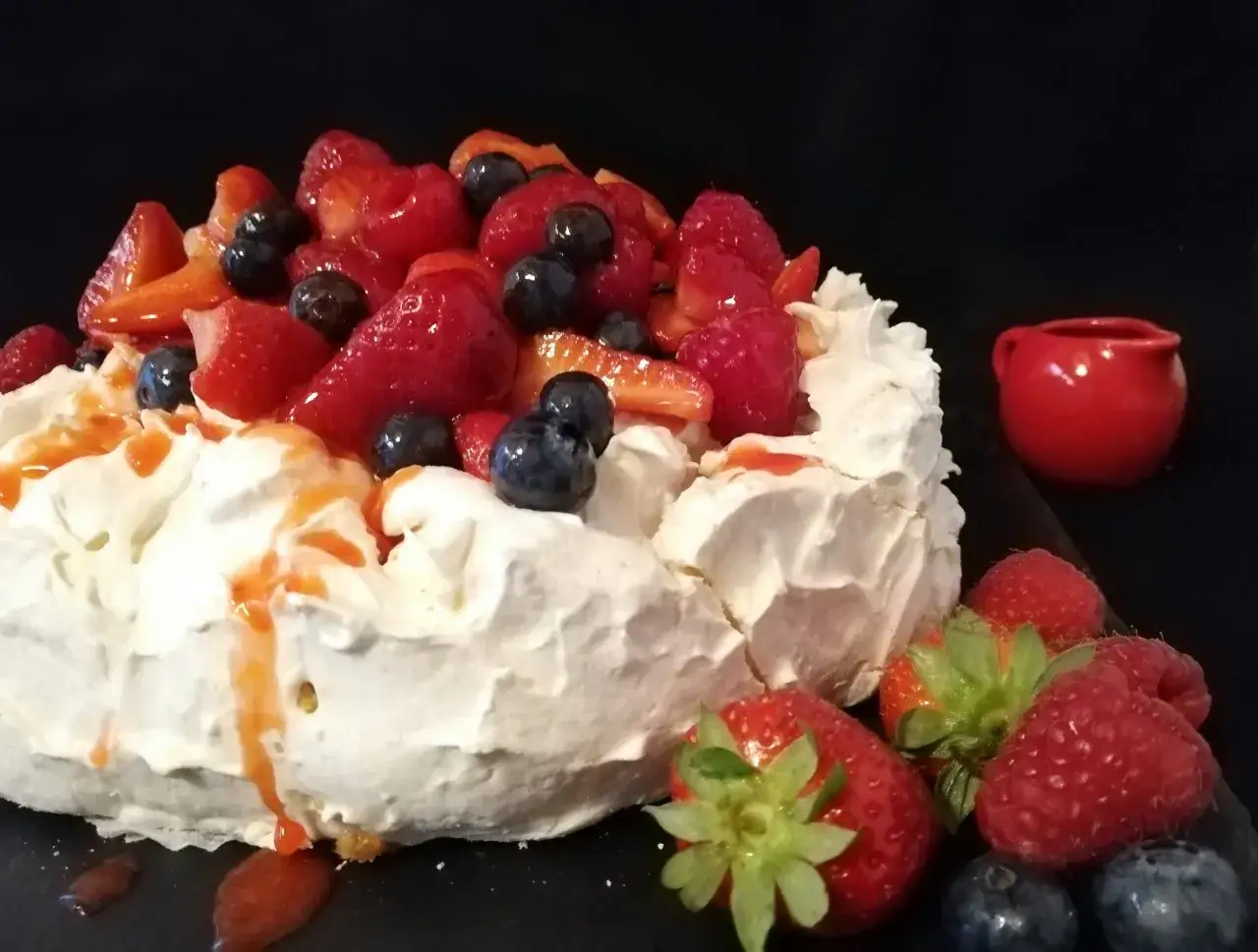 Una deliziosa torta pavlova con panna montata, fragole, mirtilli e lamponi, guarnita con salsa rossa.