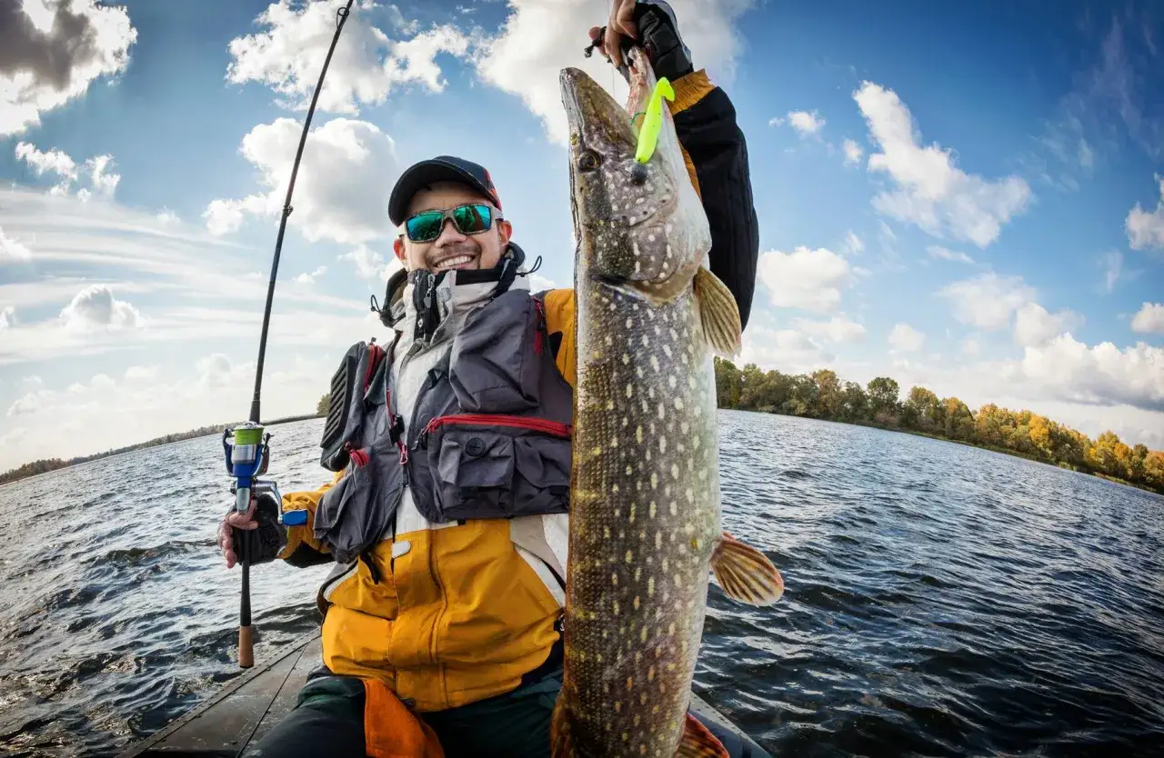 Glücklicher Angler präsentiert stolz seinen Fang beim Bodden-Angeln vom Ufer. Ein großer Hecht hängt an der Angelrute.