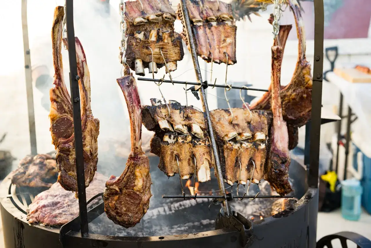 Stora k&ouml;ttstycken h&auml;nger &ouml;ver gl&ouml;dande kol, en h&auml;rlig argentinsk grillfest i full g&aring;ng.