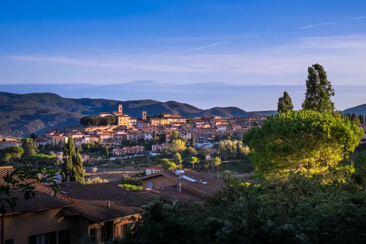 Panoramica di Montescudaio, borgo toscano con torri e tetti rossi, incastonato tra colline verdi e un cielo azzurro. Cosa vedere in questo incantevole paesaggio.