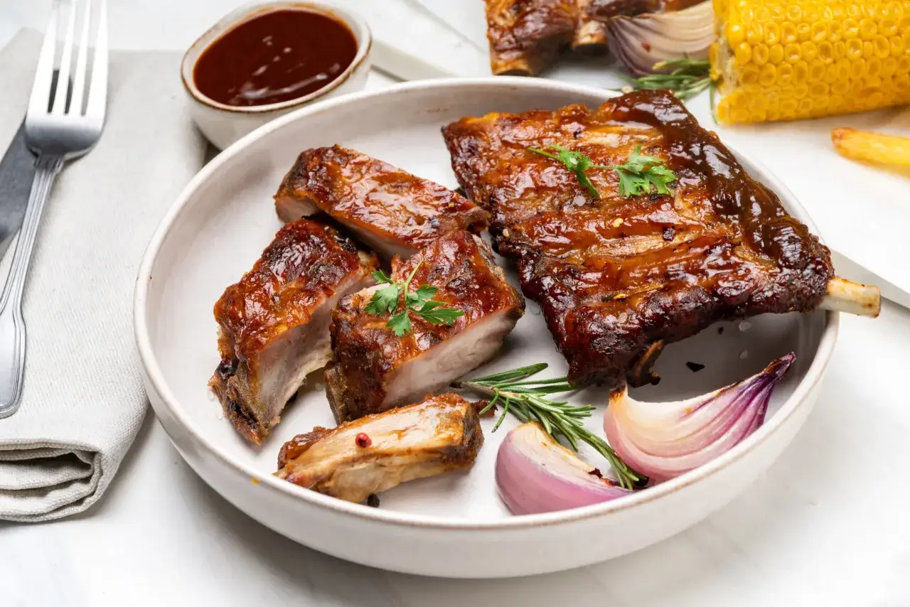 Soczyste żeberka na grilla, idealnie przyrządzone, podane z sosem BBQ, pieczoną cebulą i kukurydzą.