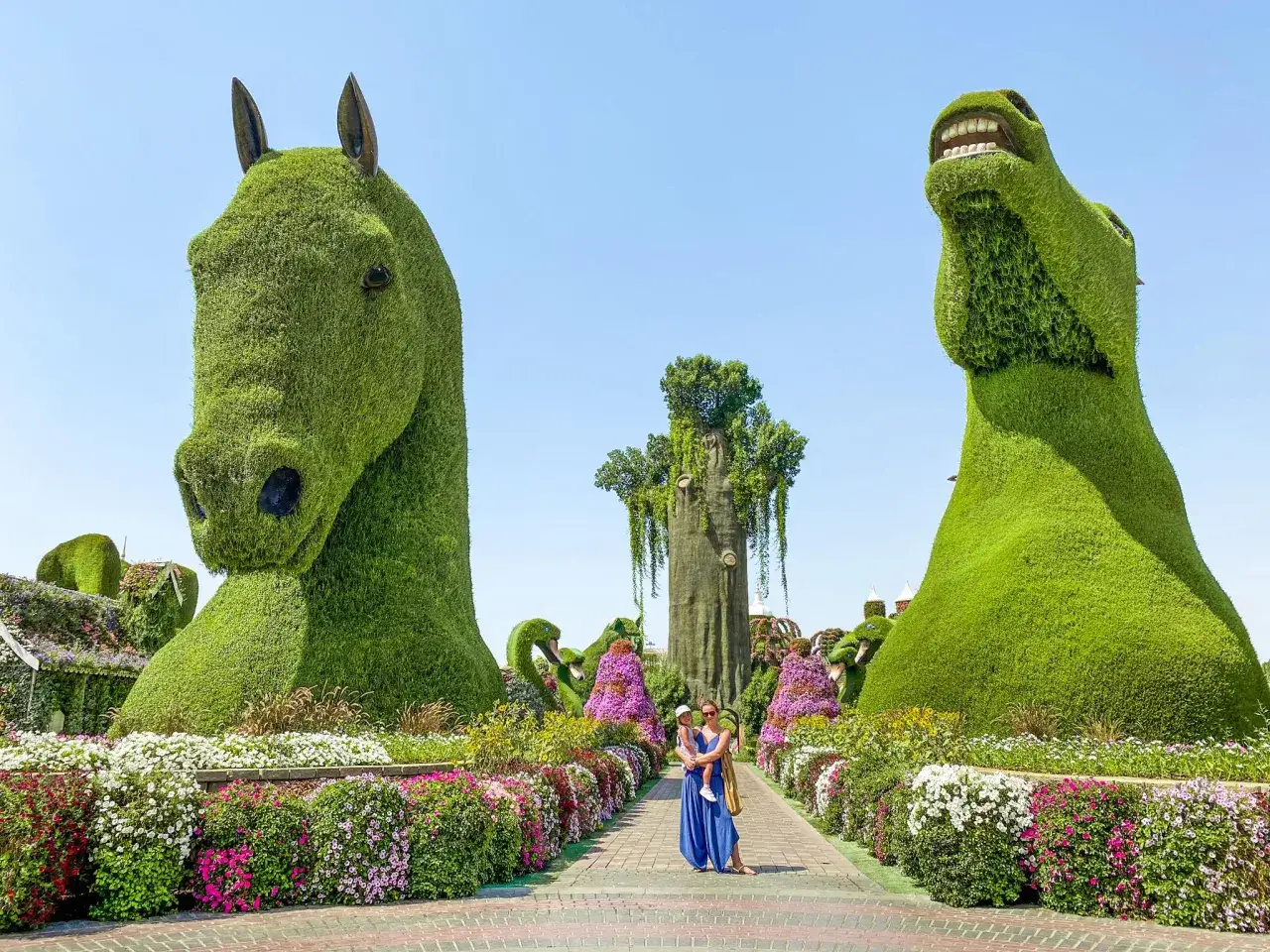 Rodzina podziwia rzeźby z żywopłotu w Miracle Garden w Dubaju. Dwa ogromne konie z zieleni i kolorowe kwiaty tworzą magiczną scenerię.