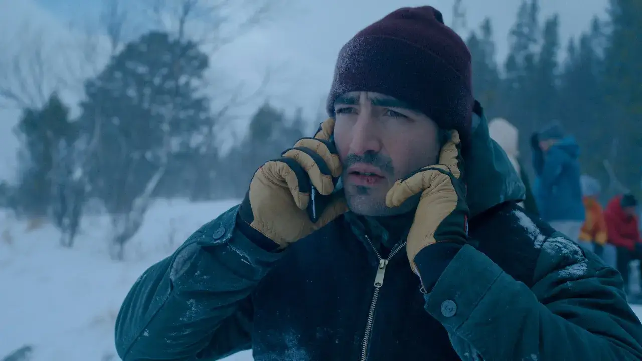 Mann mit blutiger Lippe telefoniert im Schnee, typisch für **nordic noir**. Im Hintergrund verschwommene Gestalten und Bäume.