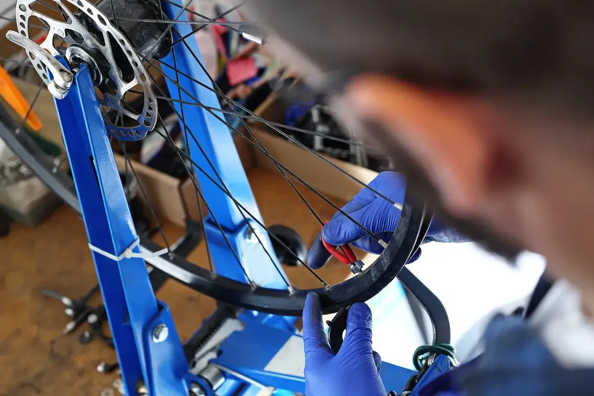 Mechanik w niebieskich rękawiczkach centruje koło roweru. Dowiedz się, ile kosztuje centrowanie koła w rowerze.