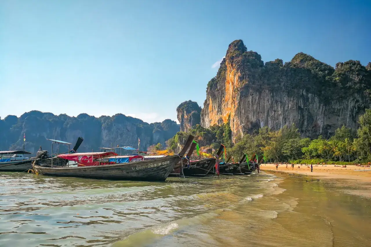 Krabi co zobaczyć: łodzie typu longtail przy plaży z wapiennymi klifami w tle.