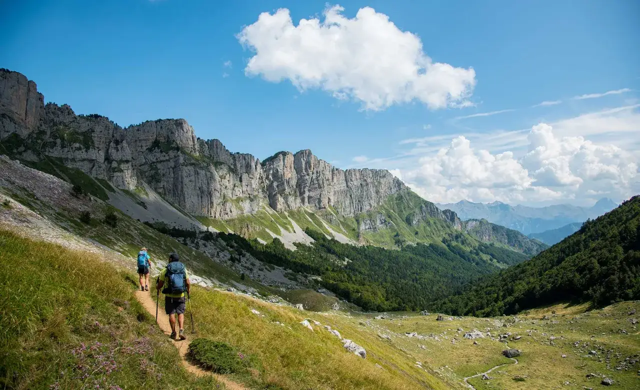 Deux randonneurs explorent un sentier de montagne spectaculaire, avec des falaises imposantes et une vallée verdoyante. Une belle rando pays basque.