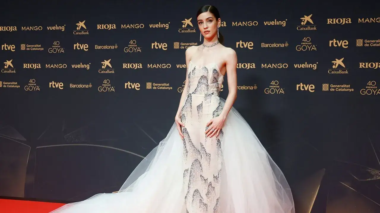 Una joven desfila en la goya alfombra roja con un vestido de tul blanco y detalles plateados.