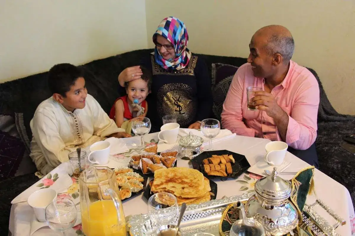 Une famille partage un repas festif. Que faire le jour de l'Aid el Kebir ? Se réunir, savourer des pâtisseries et des boissons, et profiter de ces moments précieux.