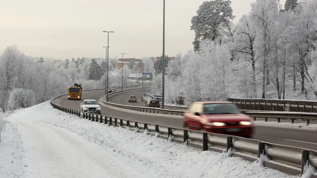 Vinterbil p&aring; en sn&ouml;t&auml;ckt motorv&auml;g. Tr&auml;den &auml;r t&auml;ckta av frost och himlen &auml;r gr&aring;.