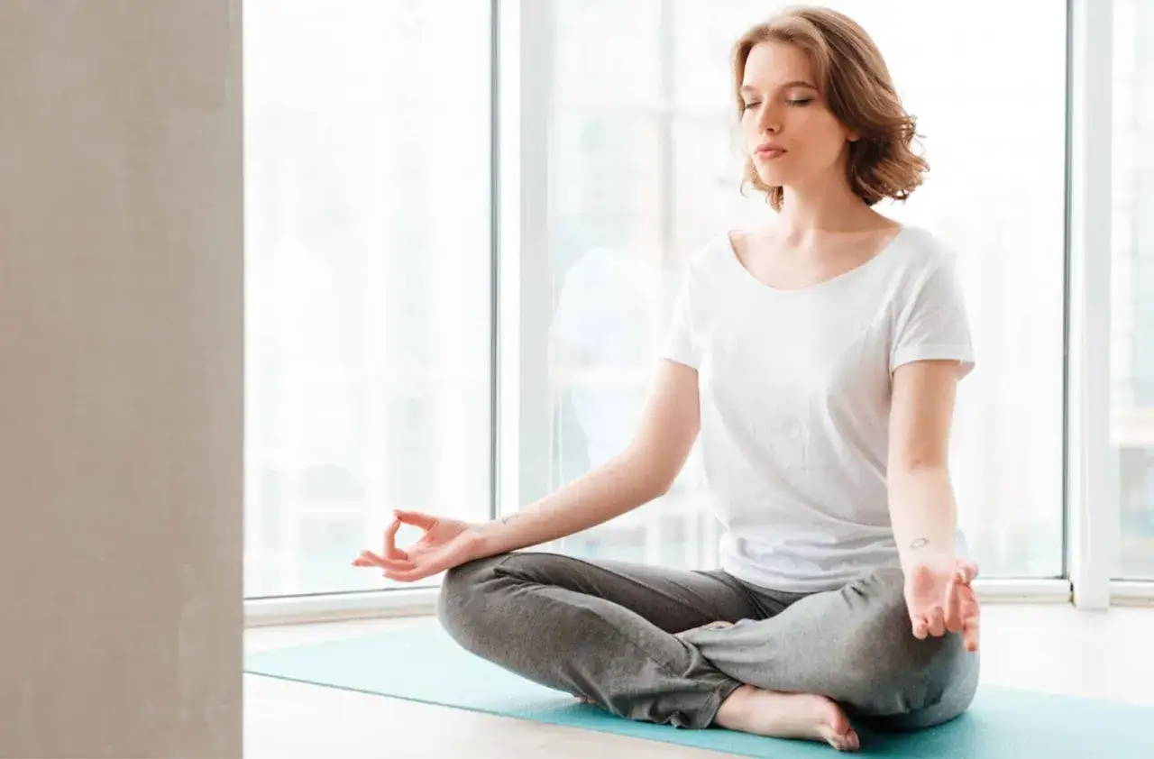 Femme en posture de lotus sur un tapis de yoga, pratiquant la respiration anti-stress. Ses yeux sont clos, elle est sereine.