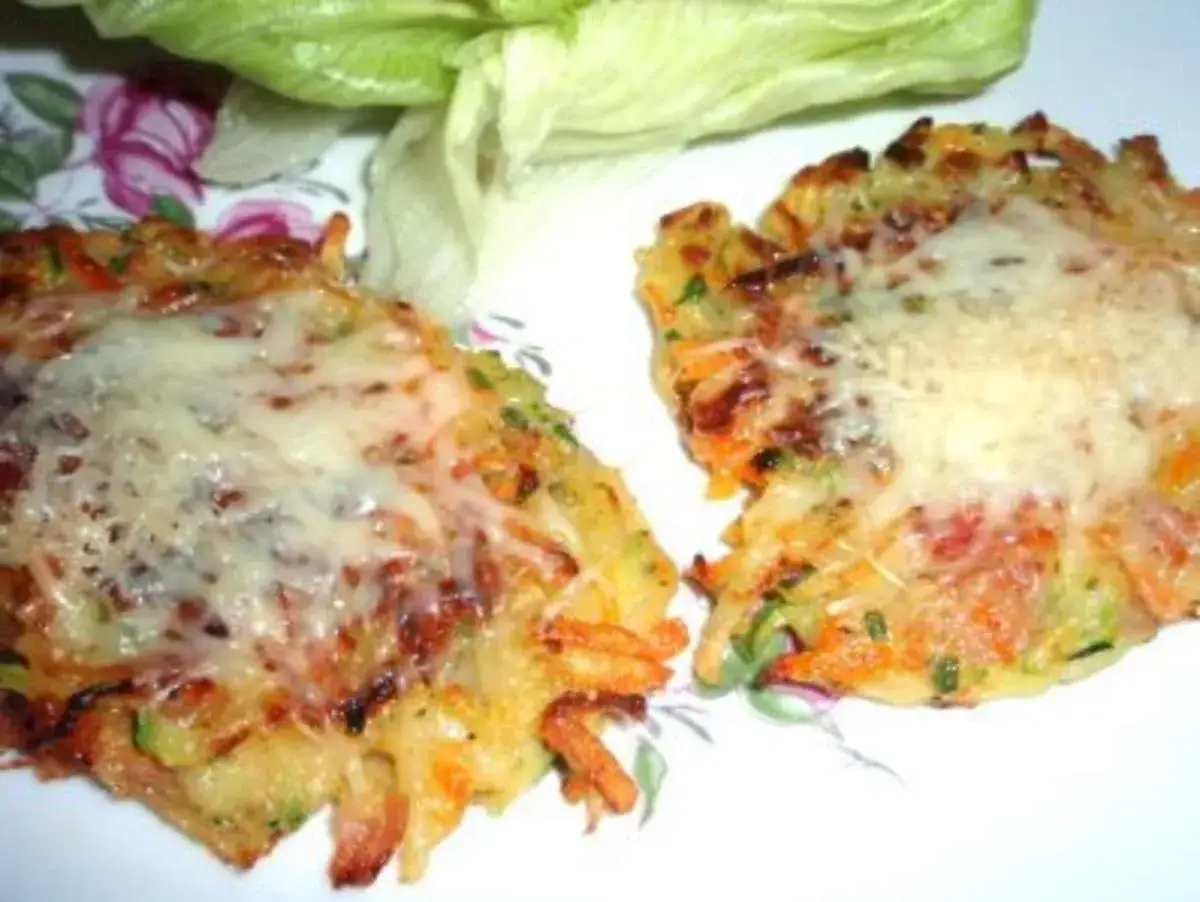 Zwei goldbraune Zucchinipuffer mit geschmolzenem Käse, serviert mit Salat. Perfekt für leichte zucchini rezepte.