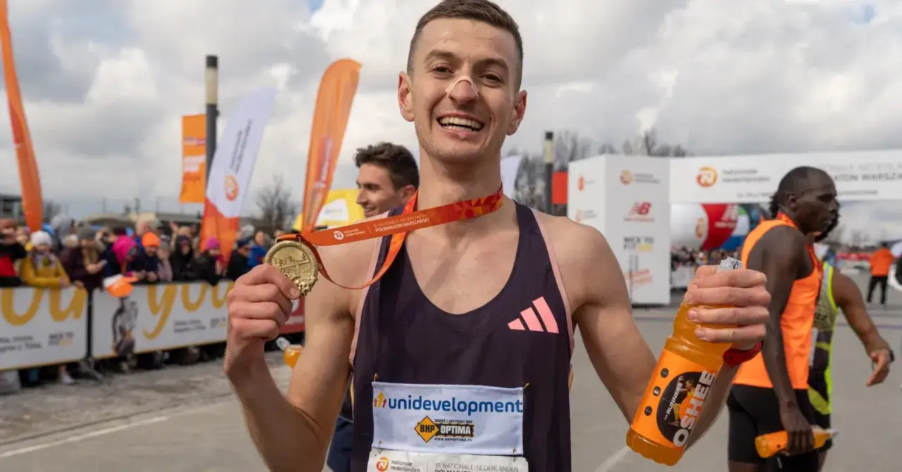 Szczęśliwy biegacz z medalem po jednym z półmaratonów w Polsce. Trzyma butelkę napoju sportowego.