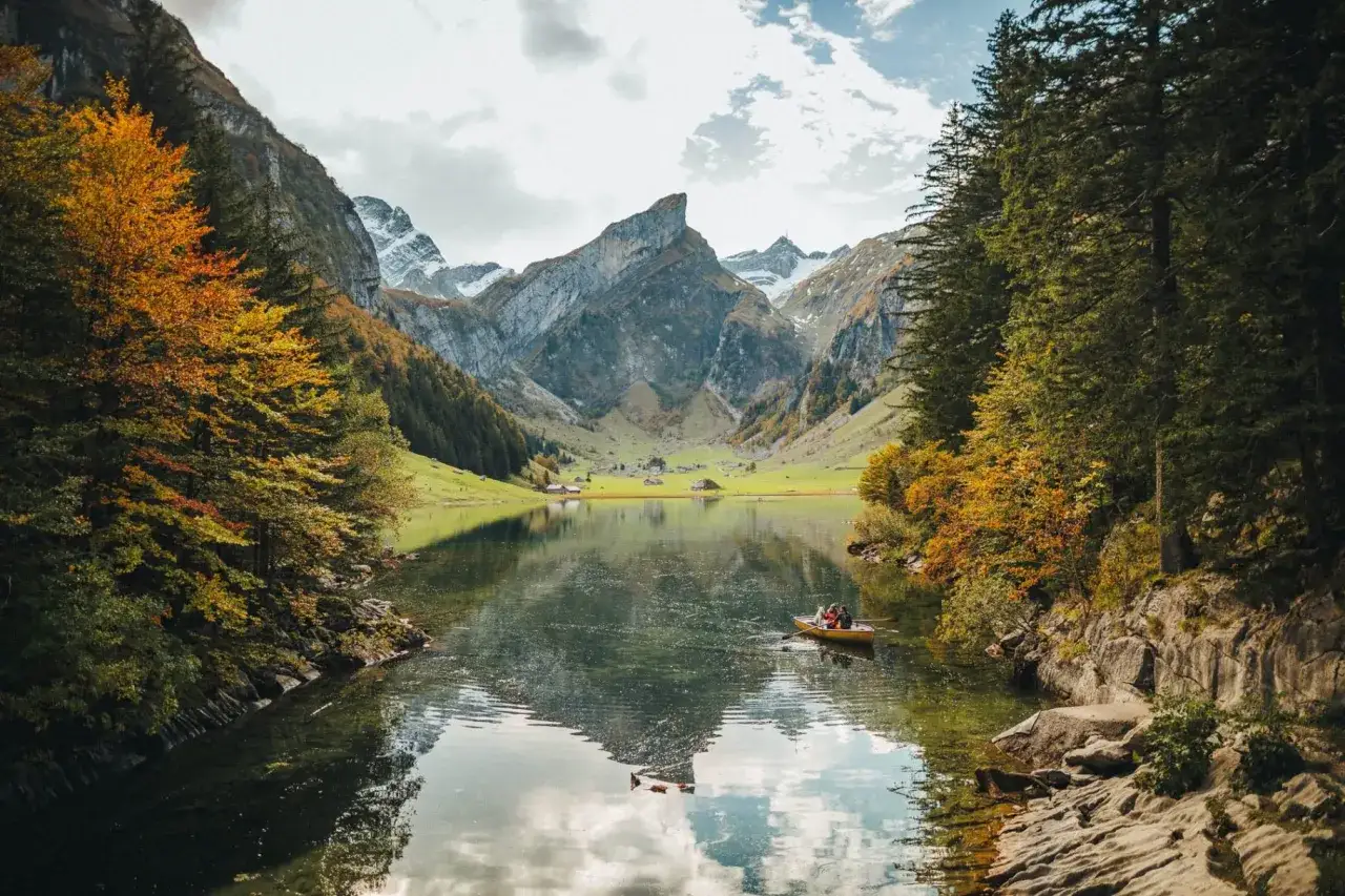 Herbstliche Seealpsee Wanderung: Ruderboot mit Menschen auf dem See, umgeben von bunten Bäumen und majestätischen Bergen.