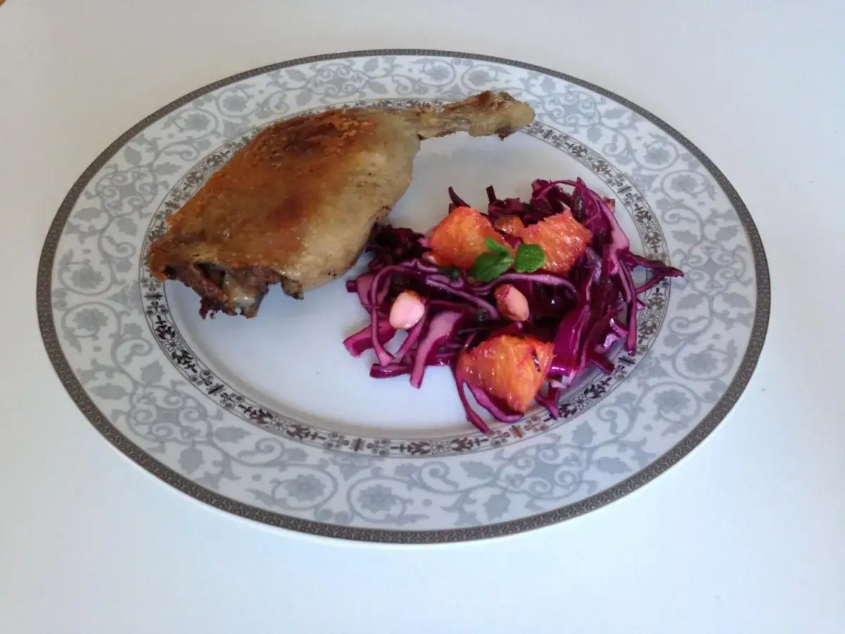 En krispig confiterad anka serveras med en rödkålssallad med apelsin och nötter på en elegant tallrik.
