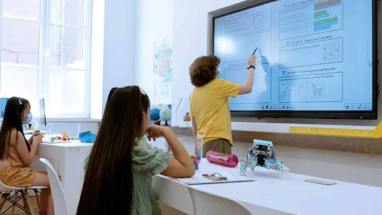 Kinder lernen an einer digitalen Tafel in der Schule. Ein Junge erkl&auml;rt etwas, w&auml;hrend zwei M&auml;dchen zuschauen.
