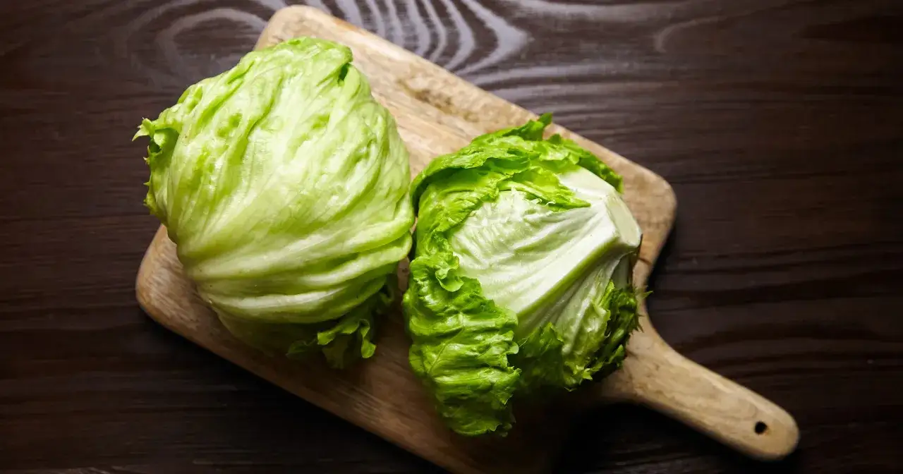 Dwie główki sałaty lodowej na desce. Czy sałata lodowa jest zdrowa? Tak, to chrupiące warzywo pełne witamin.