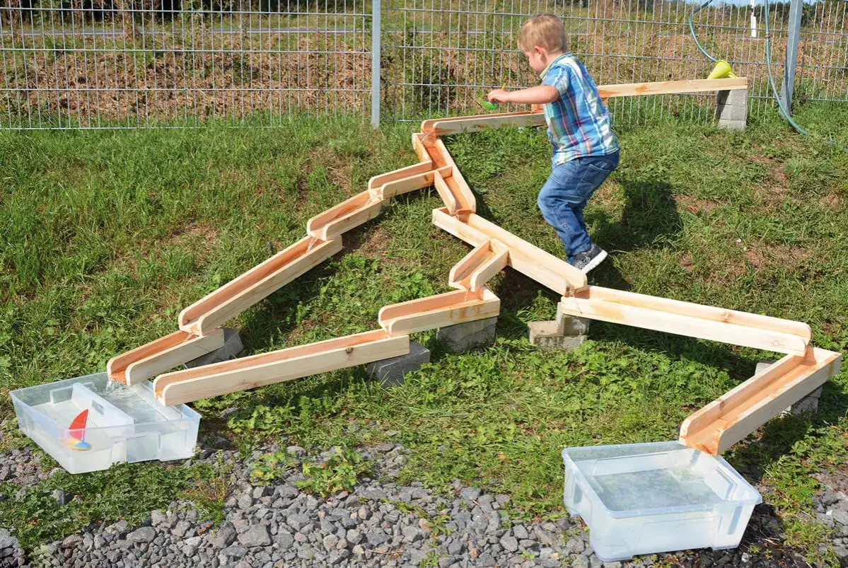 Kleiner Junge spielt mit einer Wasserrutsche im Garten. Tolle Kindergarten spiele für draußen.