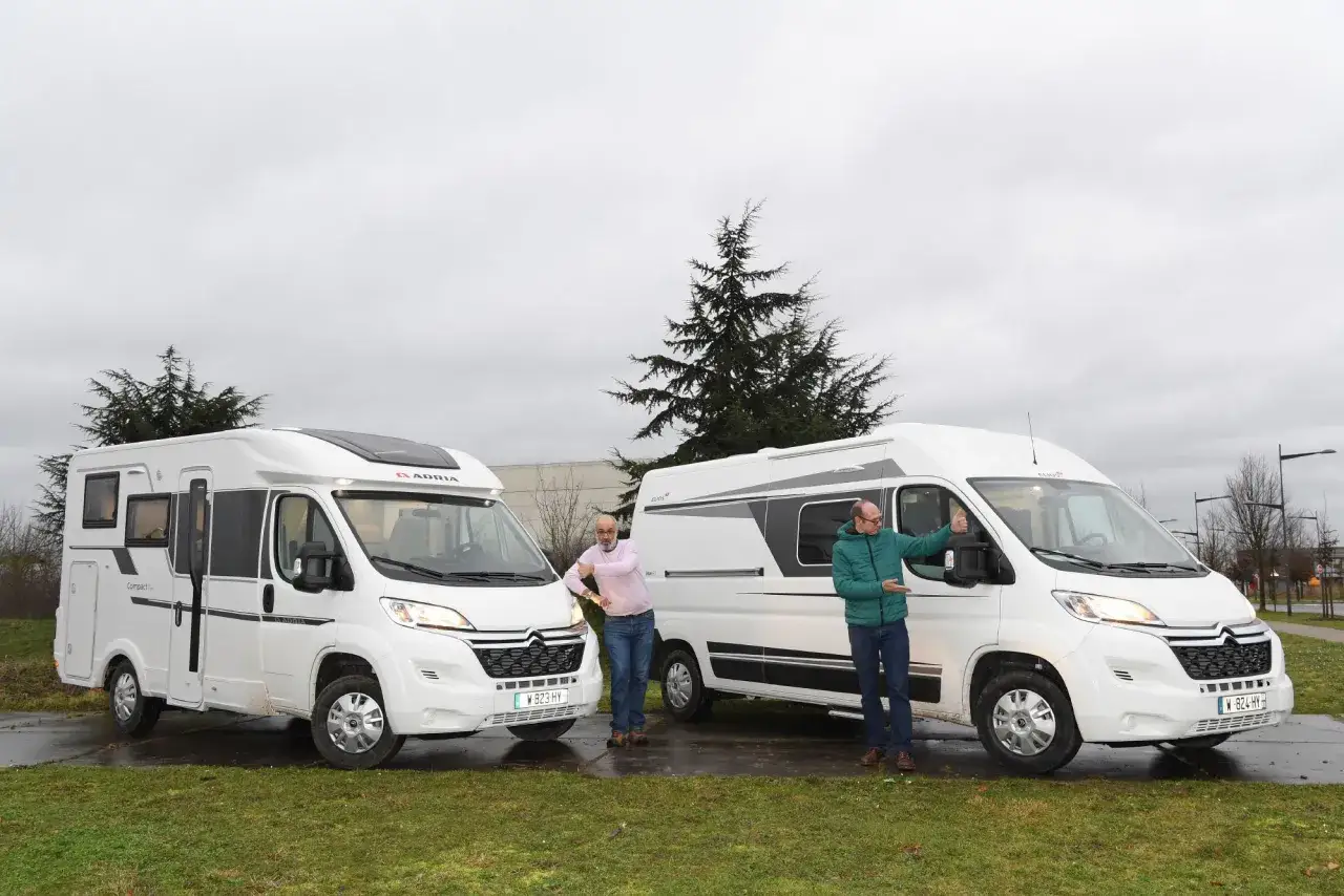 Deux hommes discutent de la largeur d'un camping-car blanc, l'un appuyé sur le véhicule de gauche, l'autre près de celui de droite.