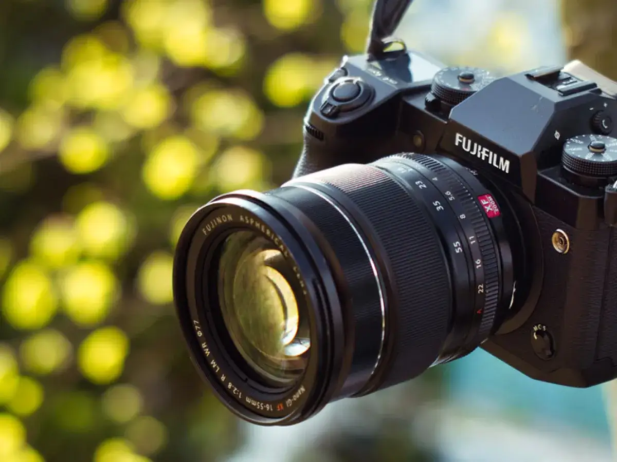 Aparat Fujifilm X-H1 z obiektywem Fujinon 16-55mm f/2.8, gotowy do uchwycenia pięknych chwil na tle rozmytego, zielonego tła.