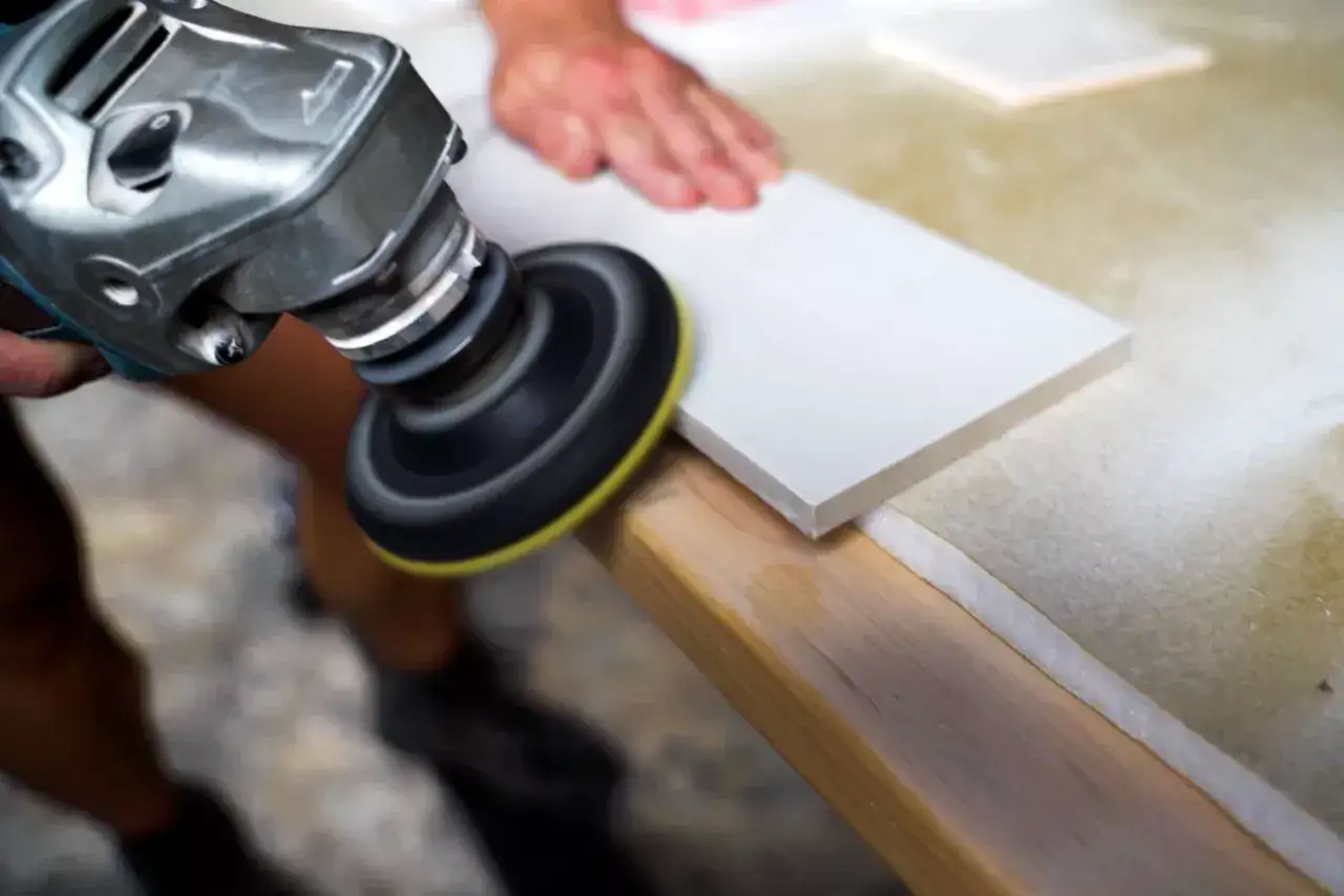 A person uses an angle grinder with a diamond wheel to cut a white tile, demonstrating how to cut tile that is already installed.