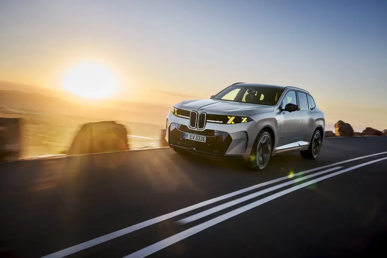 Nowe BMW X5 mknie po pustej drodze o zachodzie słońca, ukazując swoją nowoczesną sylwetkę.