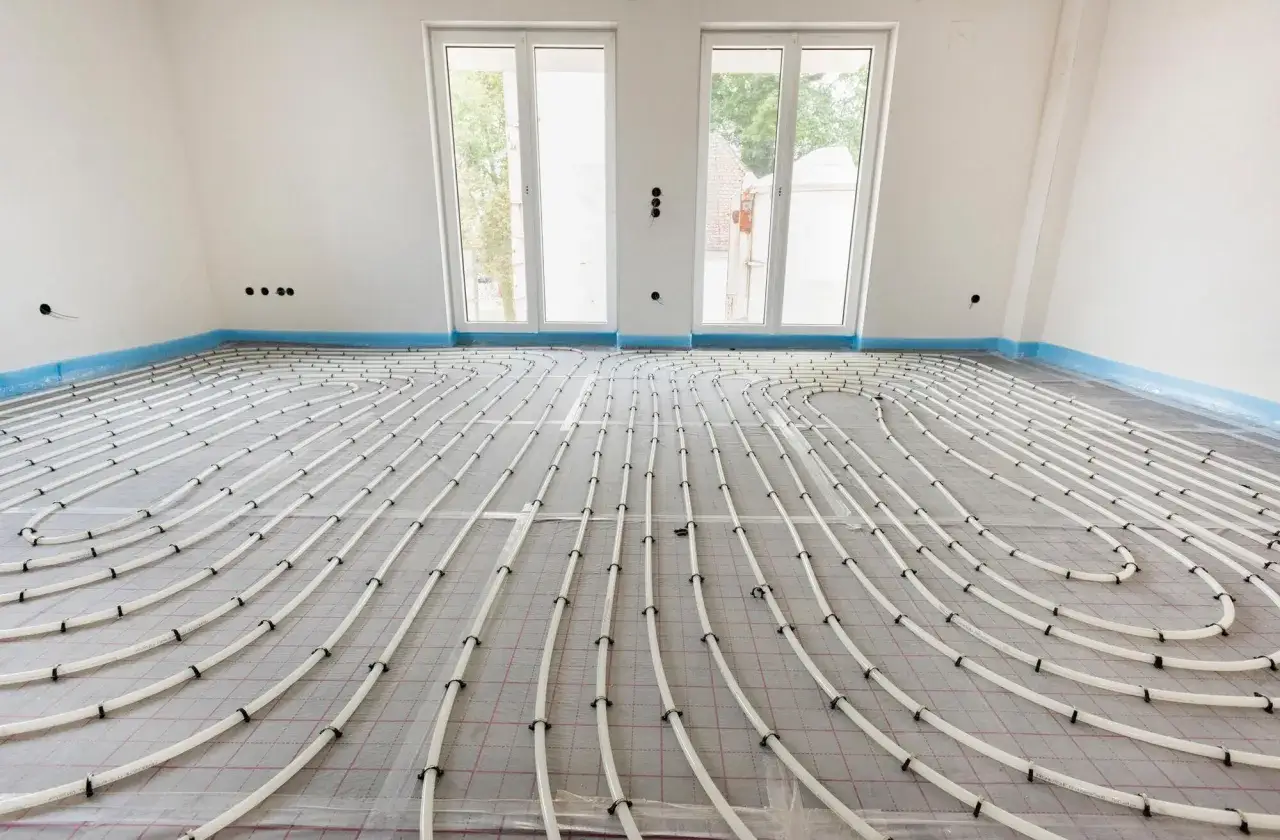 Instalación de **suelo radiante aerotermia** en una habitación en construcción. Tubos blancos serpentean sobre una malla gris, listos para ser cubiertos.
