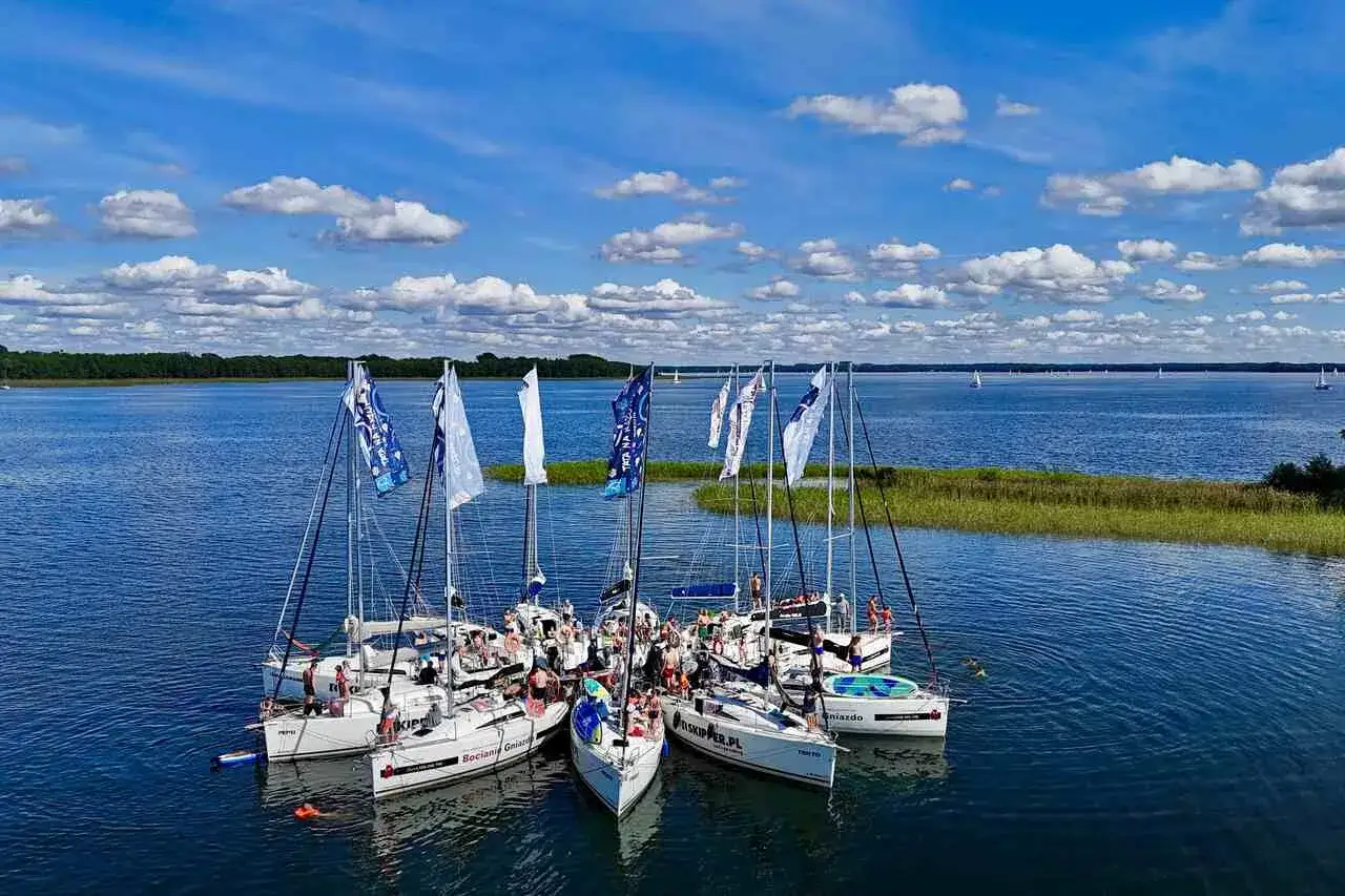 Żaglówki na Mazurach, idealne mazury atrakcje. Ludzie na pokładach, błękitne niebo i białe chmury.