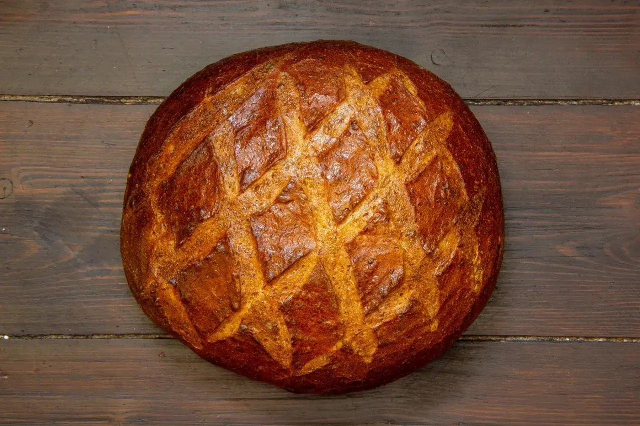 Ein goldbraunes, freigeschobenes Brot mit Rautenmuster liegt auf dunklem Holz.
