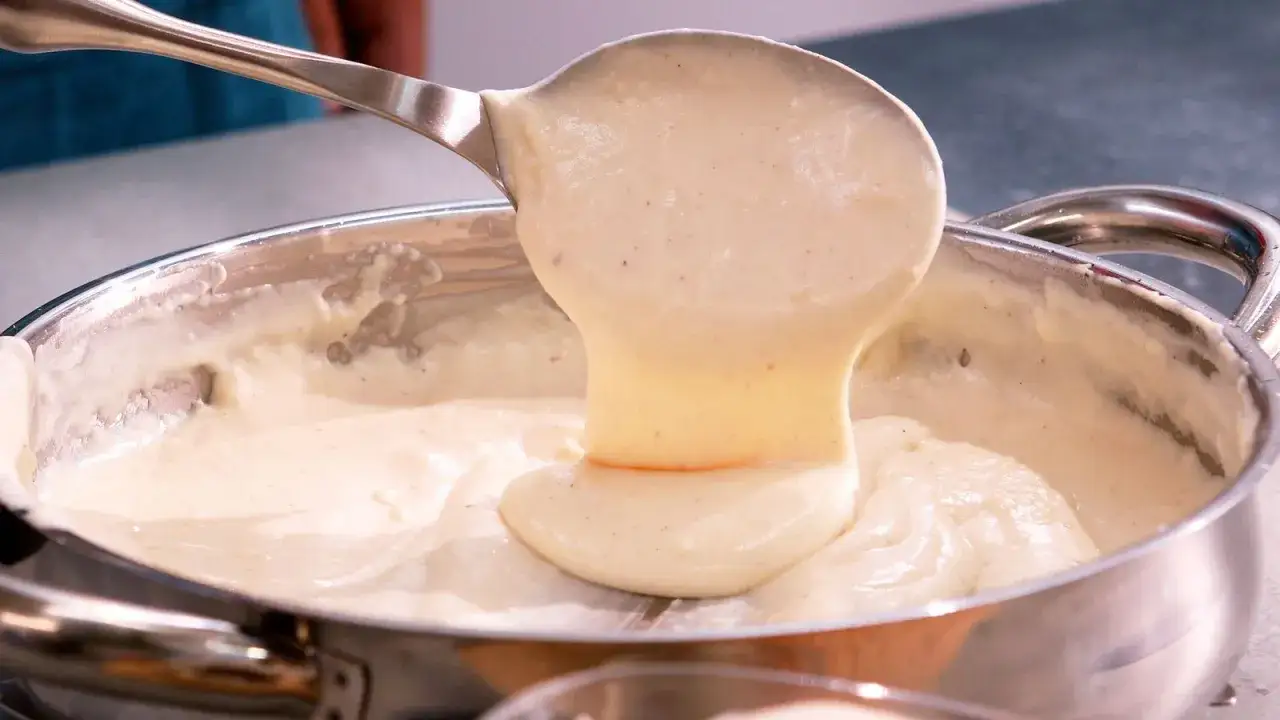Cremosa bechamel cayendo de una cuchara a una olla, perfecta para tus recetas de bechamel para lasaña.