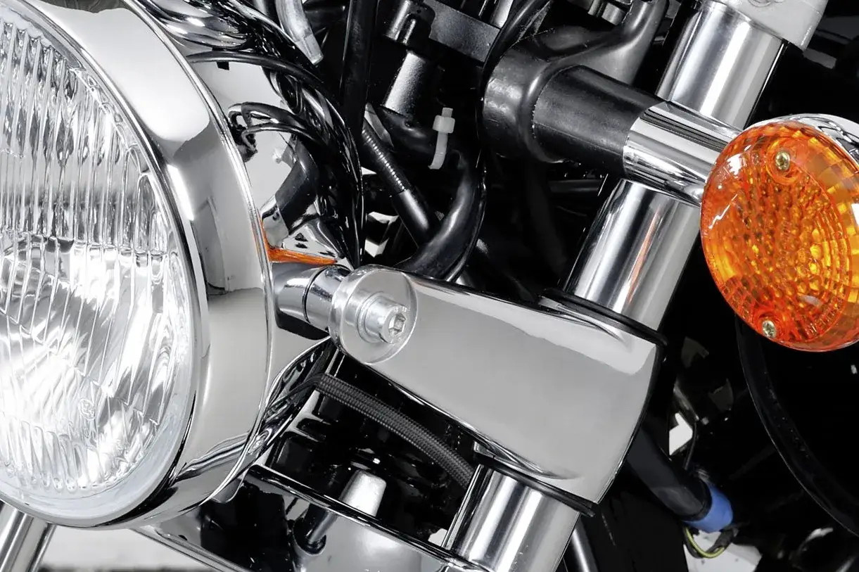 Błyszczące chromowane elementy motocykla, reflektor i pomarańczowy kierunkowskaz tworzą efekt shimmy, podkreślając klasyczny styl.