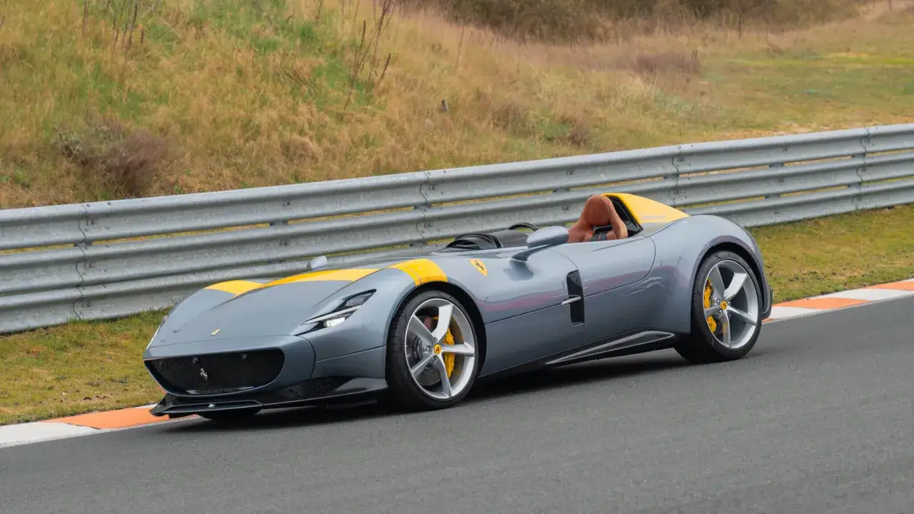 Szary Ferrari Monza SP1 z żółtym pasem na masce i żółtym wnętrzem, gotowy do jazdy po torze.