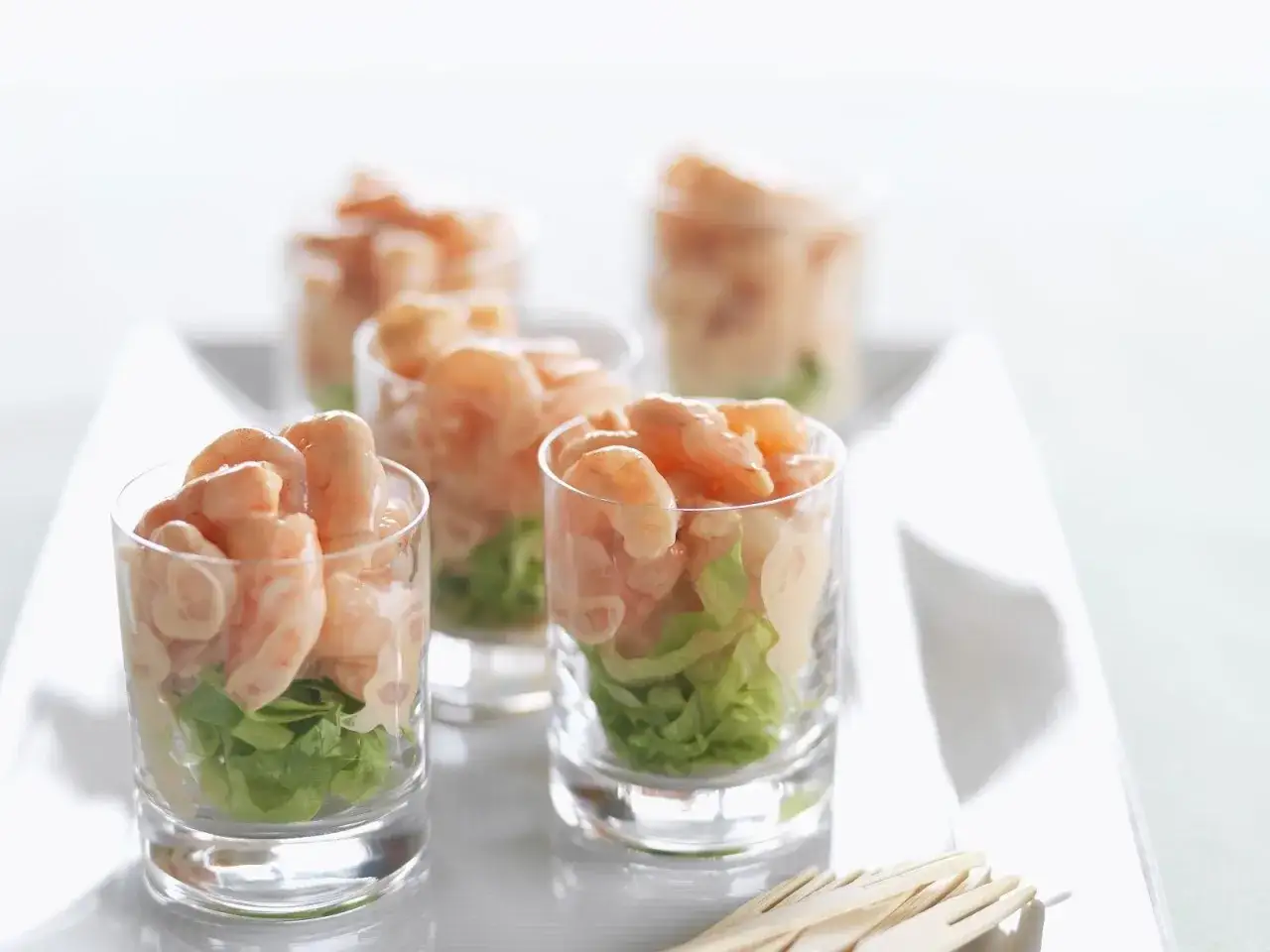 Mehrere Gläser mit Garnelen-Cocktail, gefüllt mit knackigem Salat und saftigen Garnelen, bereit zum Genießen.