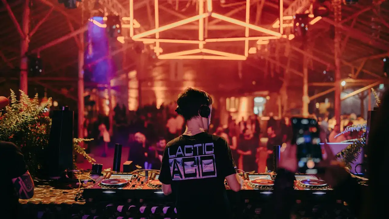 DJ w słuchawkach miksuje na imprezie techno. W tle tłum i neonowe światła. To brzmi jak występ najlepszych dj techno.