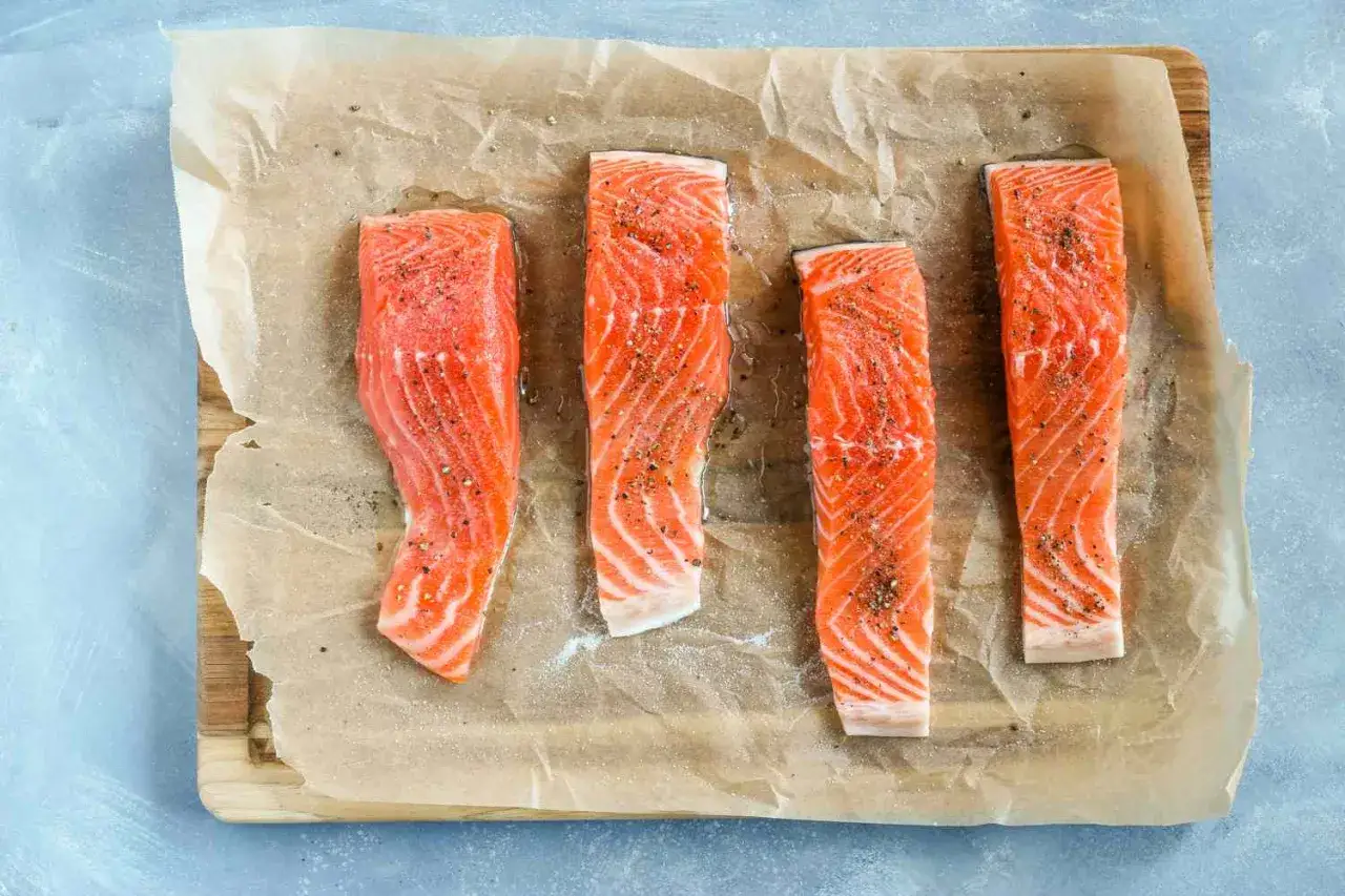 Quatre pavés de saumon crus, assaisonnés de sel et de poivre, prêts à être cuits. Une pensée pour ceux qui ont une allergie au saumon.