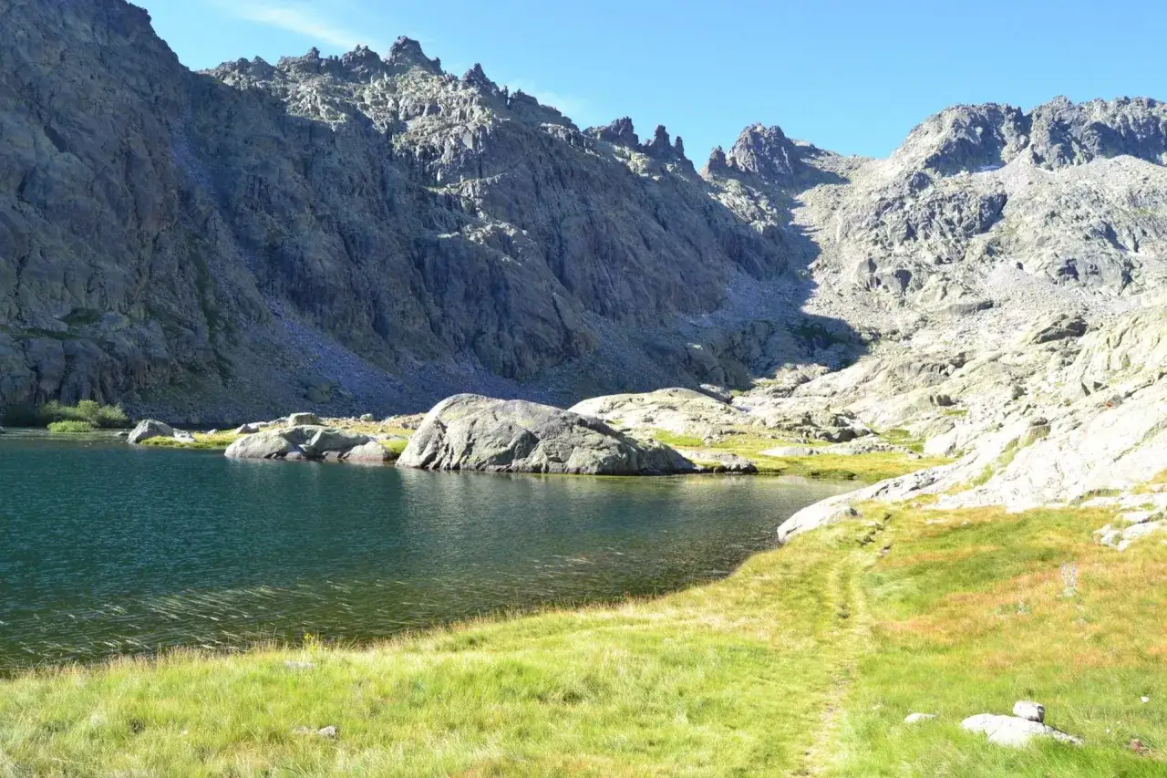 Sendero de la ruta laguna grande de Gredos. Un lago azul rodeado de rocas y montañas imponentes bajo un cielo despejado.