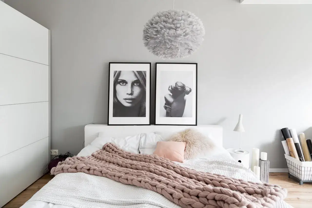 Gemütliches Schlafzimmer in Altrosa und Grau mit zwei Porträts über dem Bett und einer grob gestrickten Decke.