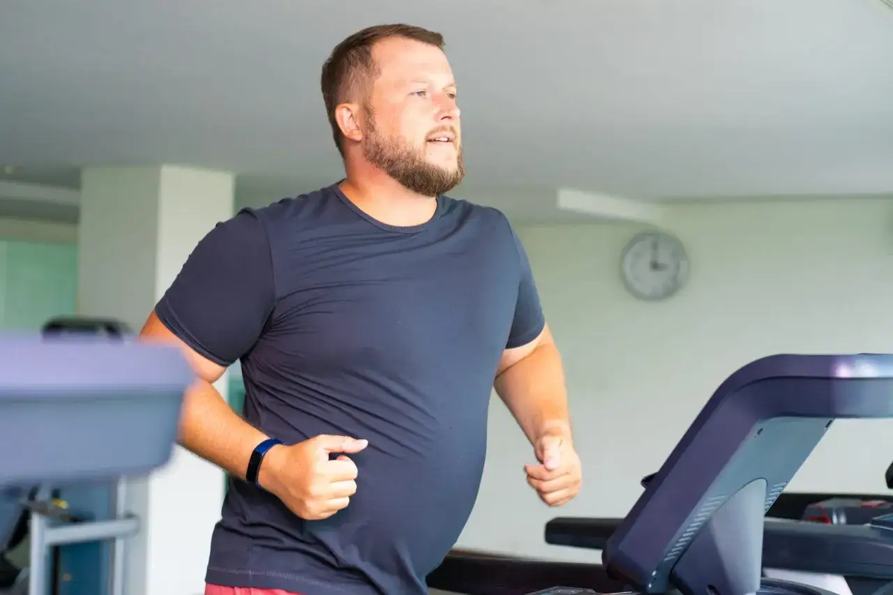 Uomo con barba corre sul tapis roulant, impegnato a eliminare il grasso addominale uomo come eliminarlo con allenamento.