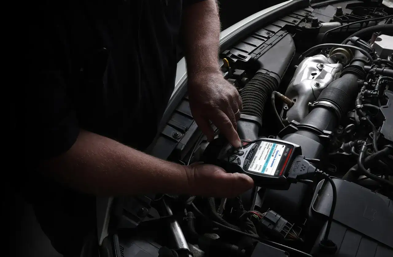 Mec&aacute;nico diagnostica un coche que se para en marcha, usando un esc&aacute;ner para leer c&oacute;digos de error del motor.