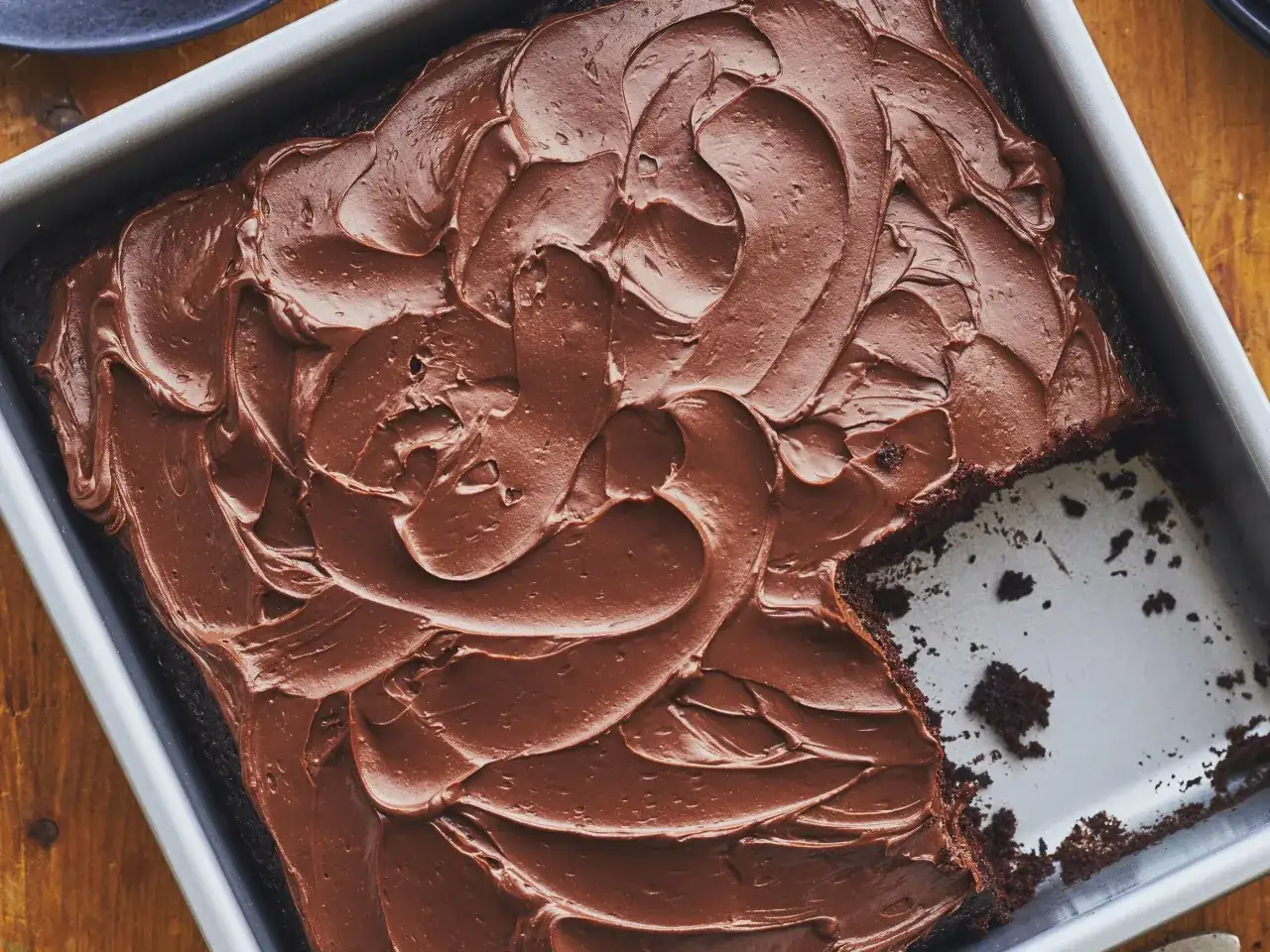Gâteau au cacao en poudre, tout juste sorti du four, avec un glaçage au chocolat onctueux. Une part a été retirée, révélant la texture moelleuse.