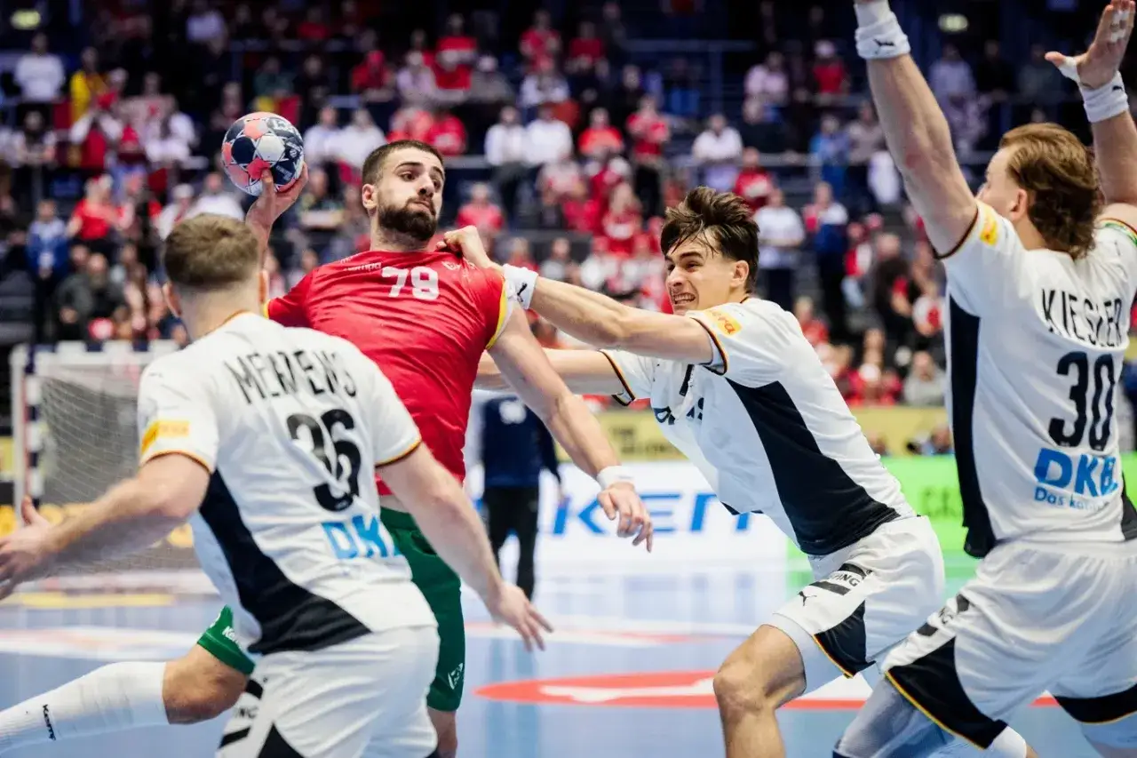 Zacięta walka na boisku! Zawodnik w czerwonej koszulce z numerem 79 próbuje rzucić piłkę, ale obrońcy z Niemiec, w białych strojach, skutecznie go blokują. Emocje w **piłka ręczna Niemcy** sięgają zenitu!
