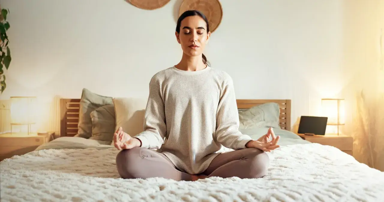 A woman meditates on a bed, a peaceful scene that illustrates how to cultivate patience through mindfulness.