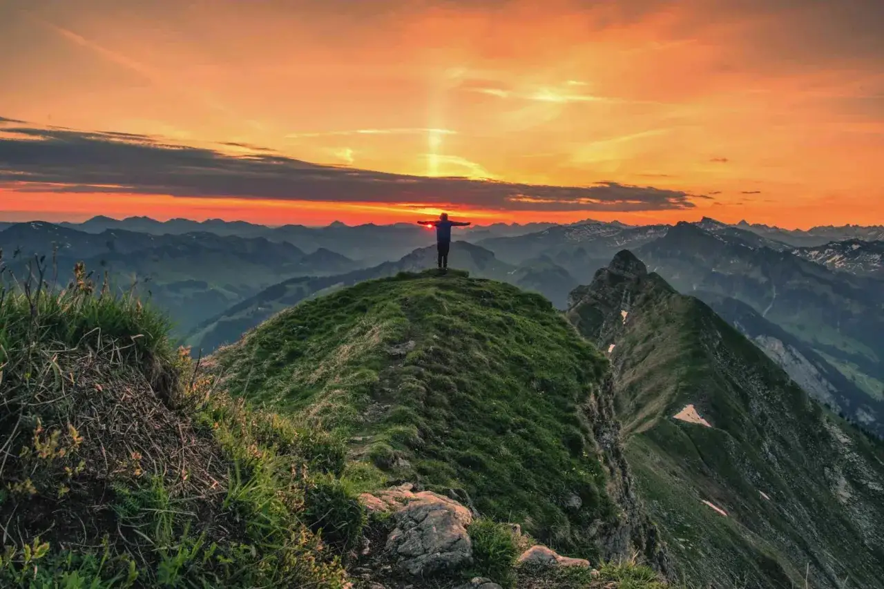 Sonnenuntergang auf der Kanisfluh Wanderung. Ein Wanderer steht mit ausgebreiteten Armen auf dem Gipfel und genie&szlig;t die atemberaubende Aussicht.