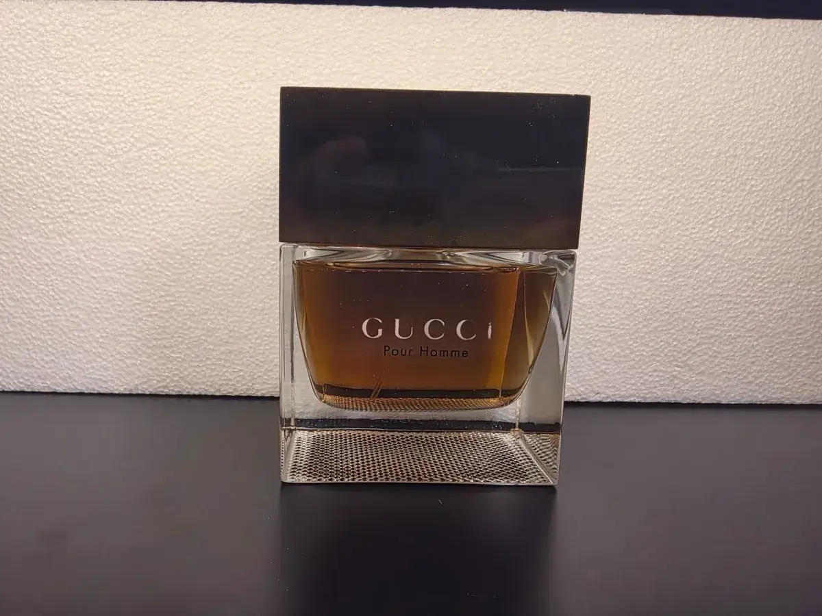 Elegancka butelka perfum Gucci Pour Homme o bursztynowym kolorze, z ciemną nakrętką.