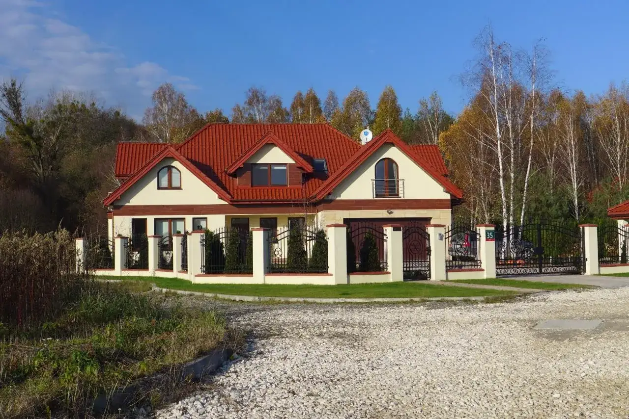 Nowoczesne projekty domów dworkowych z czerwonym dachem, otoczone zielenią i ozdobnym płotem.